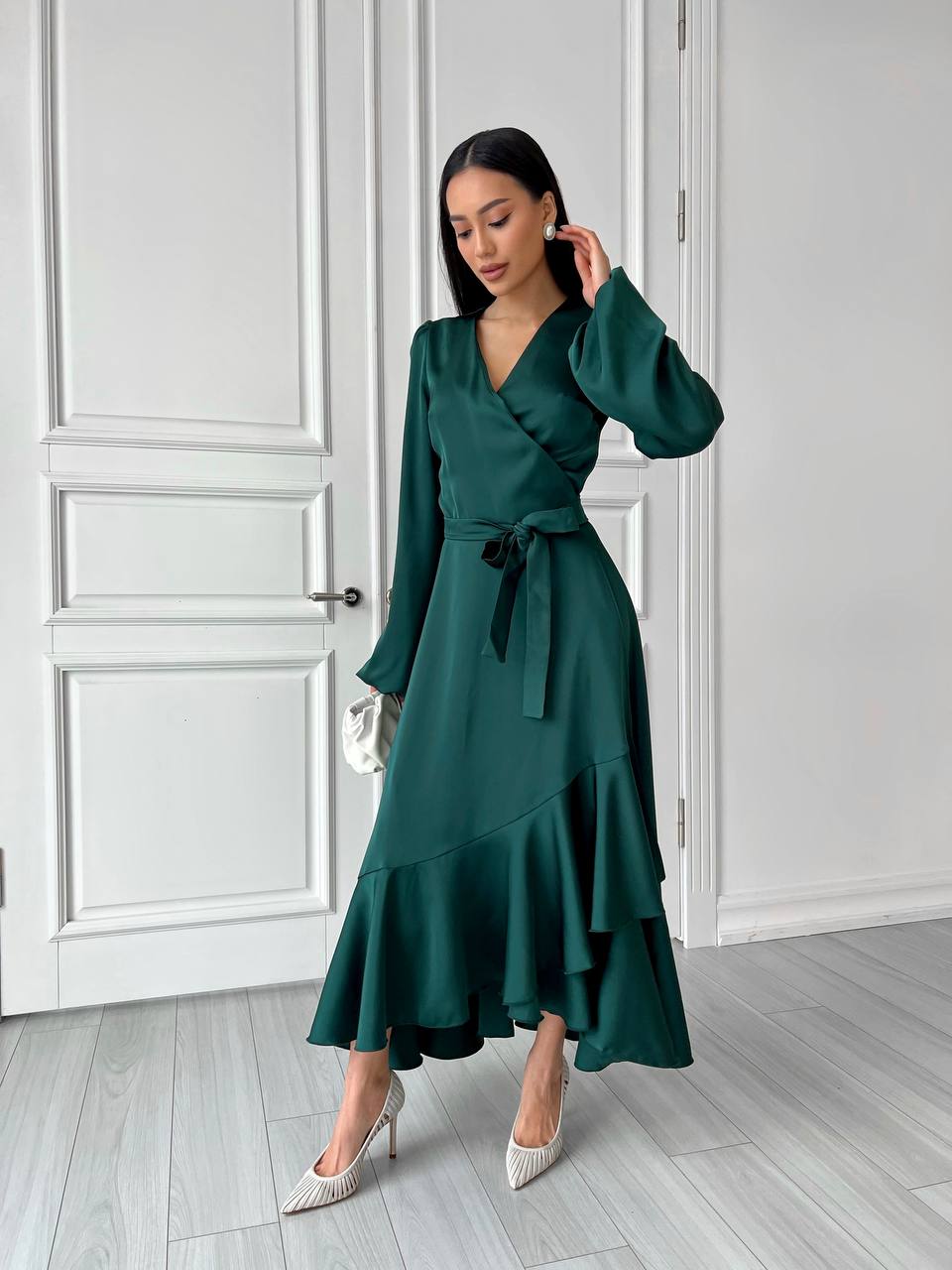 Woman wearing a green dress standing in a room with white walls and wooden floor.