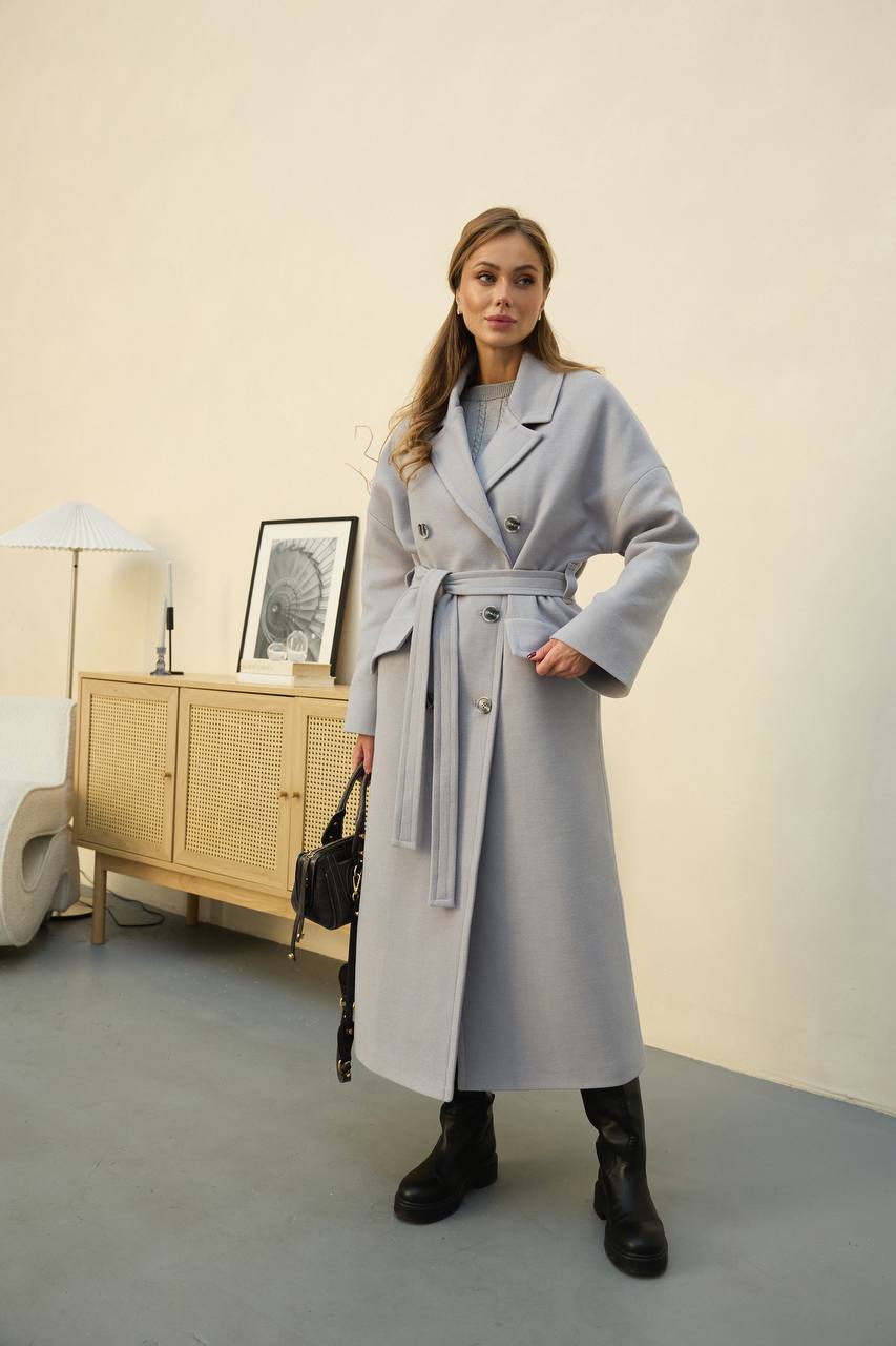 Woman wearing a long gray coat in an indoor setting.