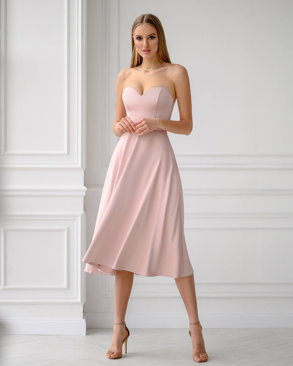 Woman wearing a pink strapless dress against a white wall