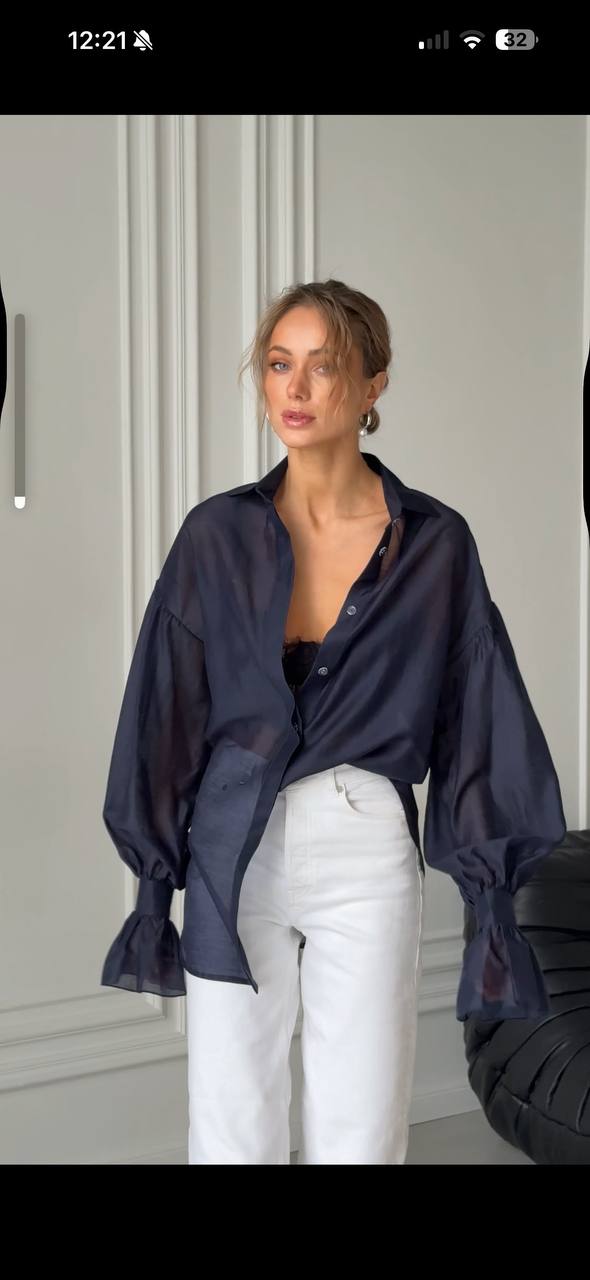 Woman wearing a navy blue shirt over a black top with white pants in a neutral setting.