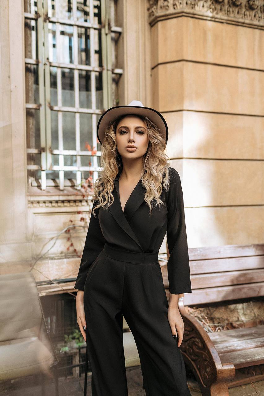 Woman in a black outfit and hat standing in front of a building with large windows.