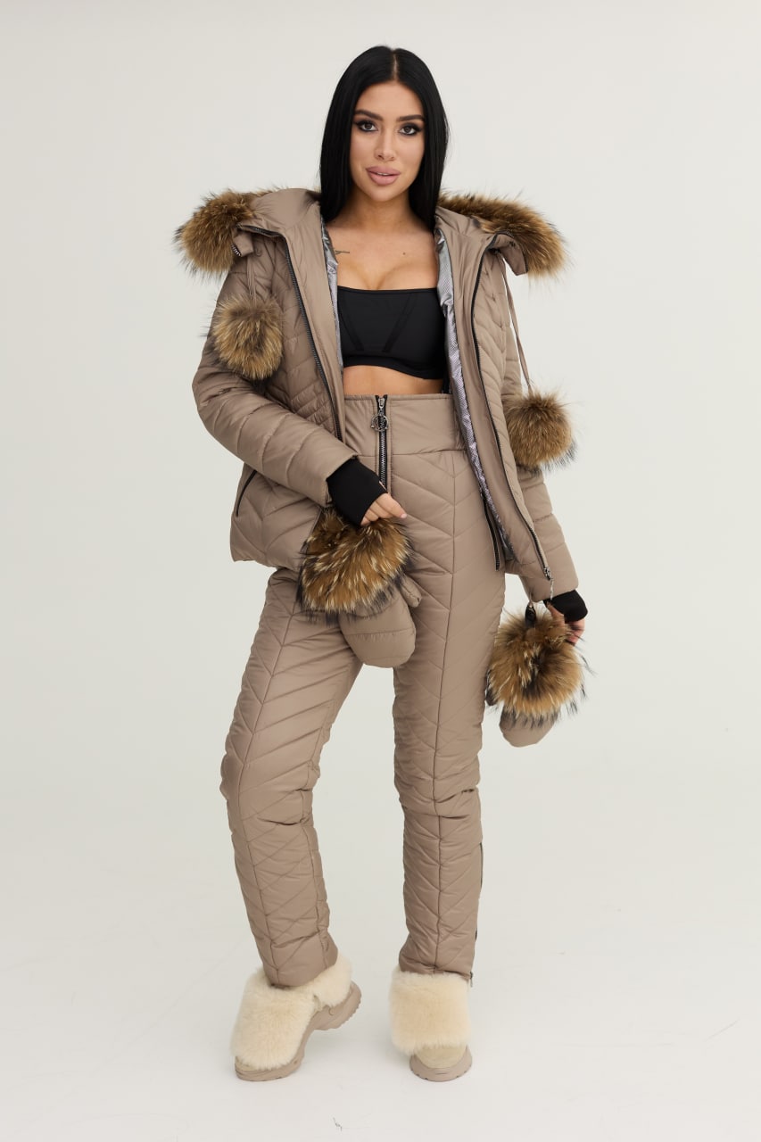 Woman wearing a beige puffer jacket with fur trim and matching pants on a white background