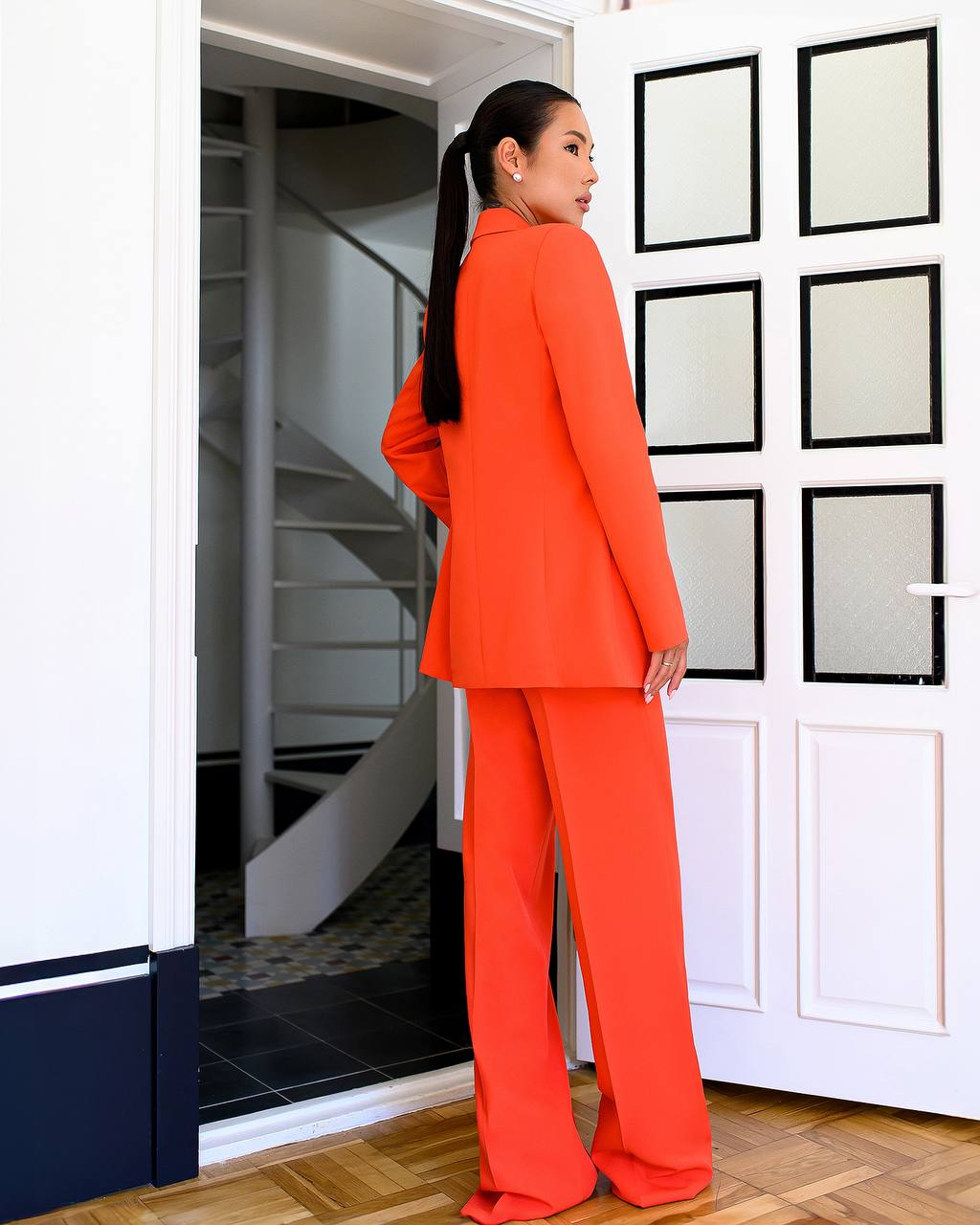 Woman in an orange outfit standing in a room with white walls and a staircase.