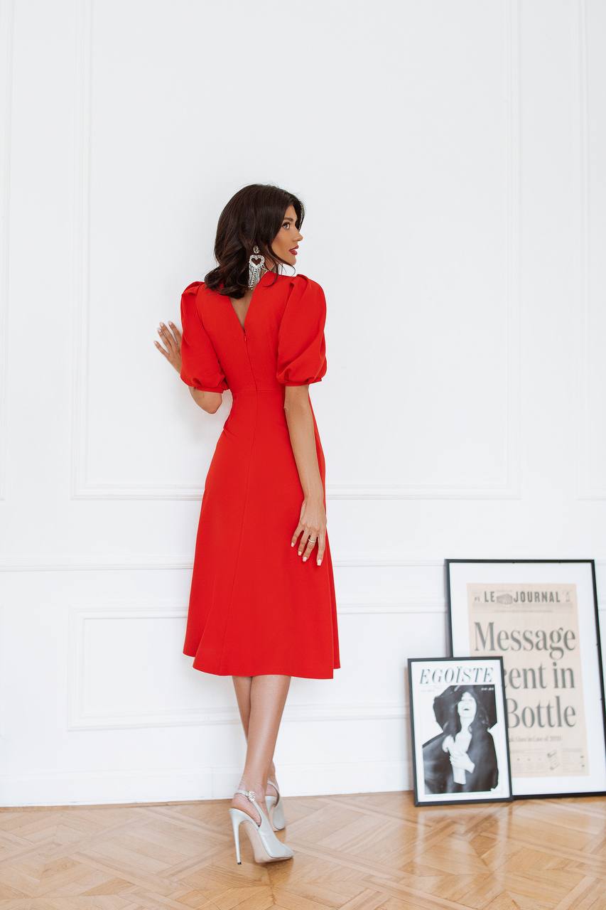 Woman in a red dress standing in a room with framed pictures on the wall.