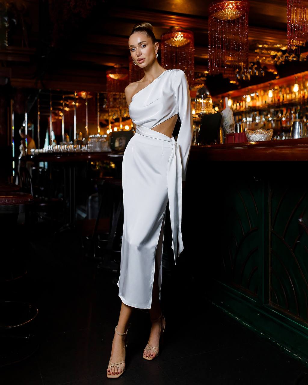 Woman in a white dress standing in a dimly lit bar.
