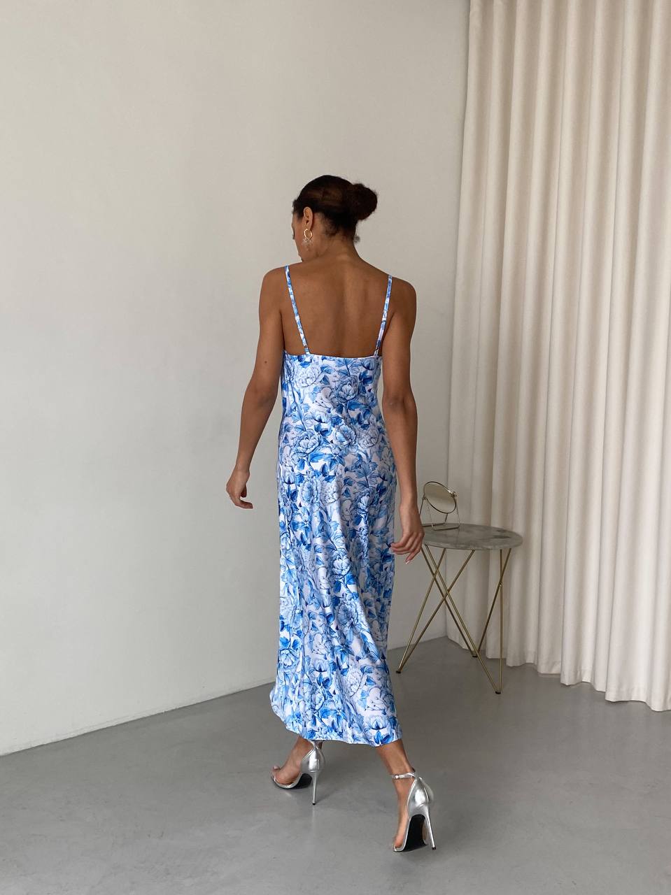 Woman wearing a blue floral dress standing in a minimalistic room with white walls and a gray floor.