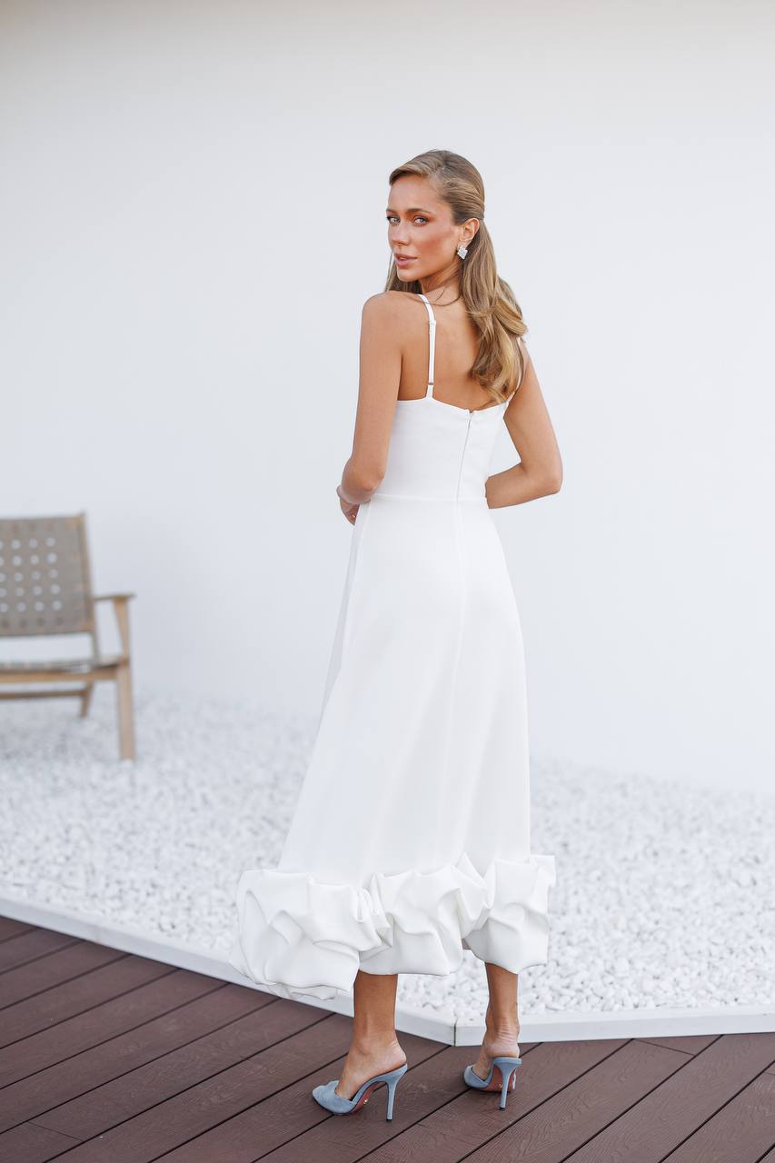 Woman in a white dress standing on a wooden deck with a white wall background