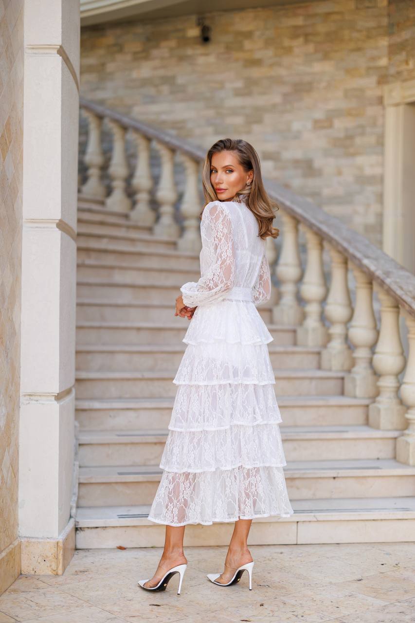 Woman in a white lace dress standing on stone steps with a stone wall background