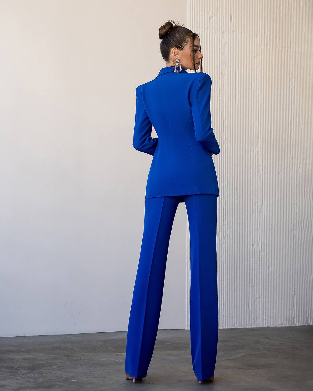 Woman wearing a blue suit standing against a plain wall.