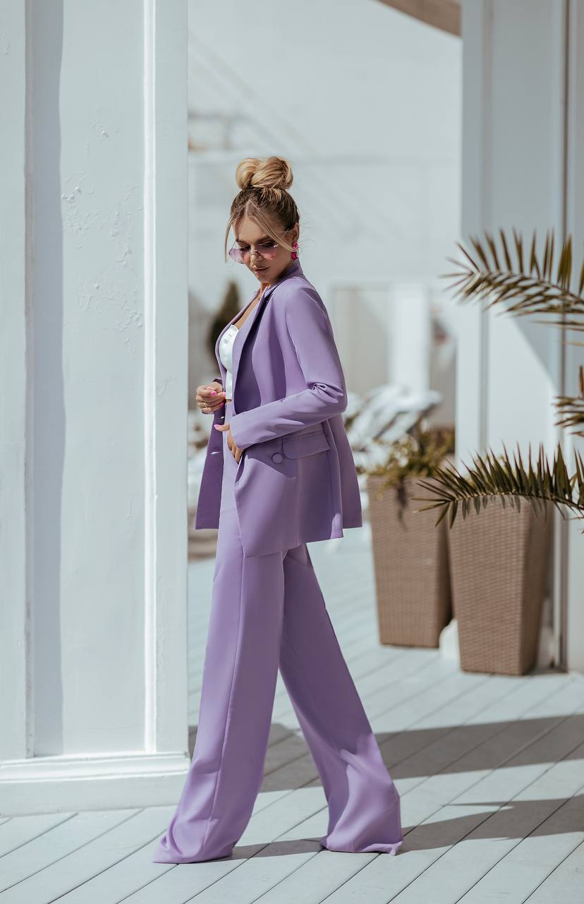 Woman in a lavender suit standing on a wooden deck with plants in the background