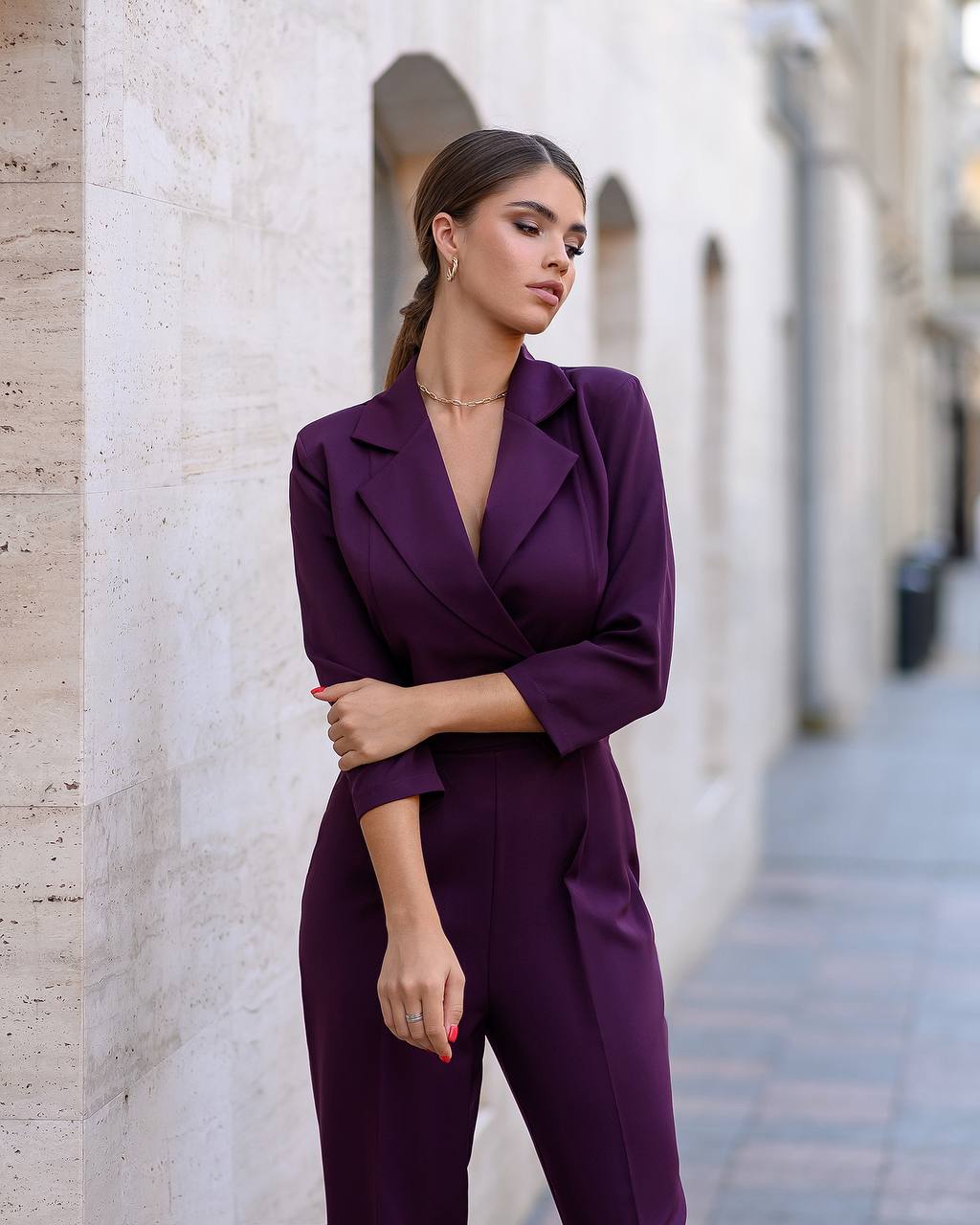 Woman wearing a purple suit standing against a light-colored wall.