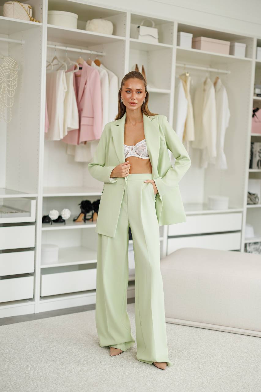 Woman in a light green suit standing in a well-organized wardrobe.