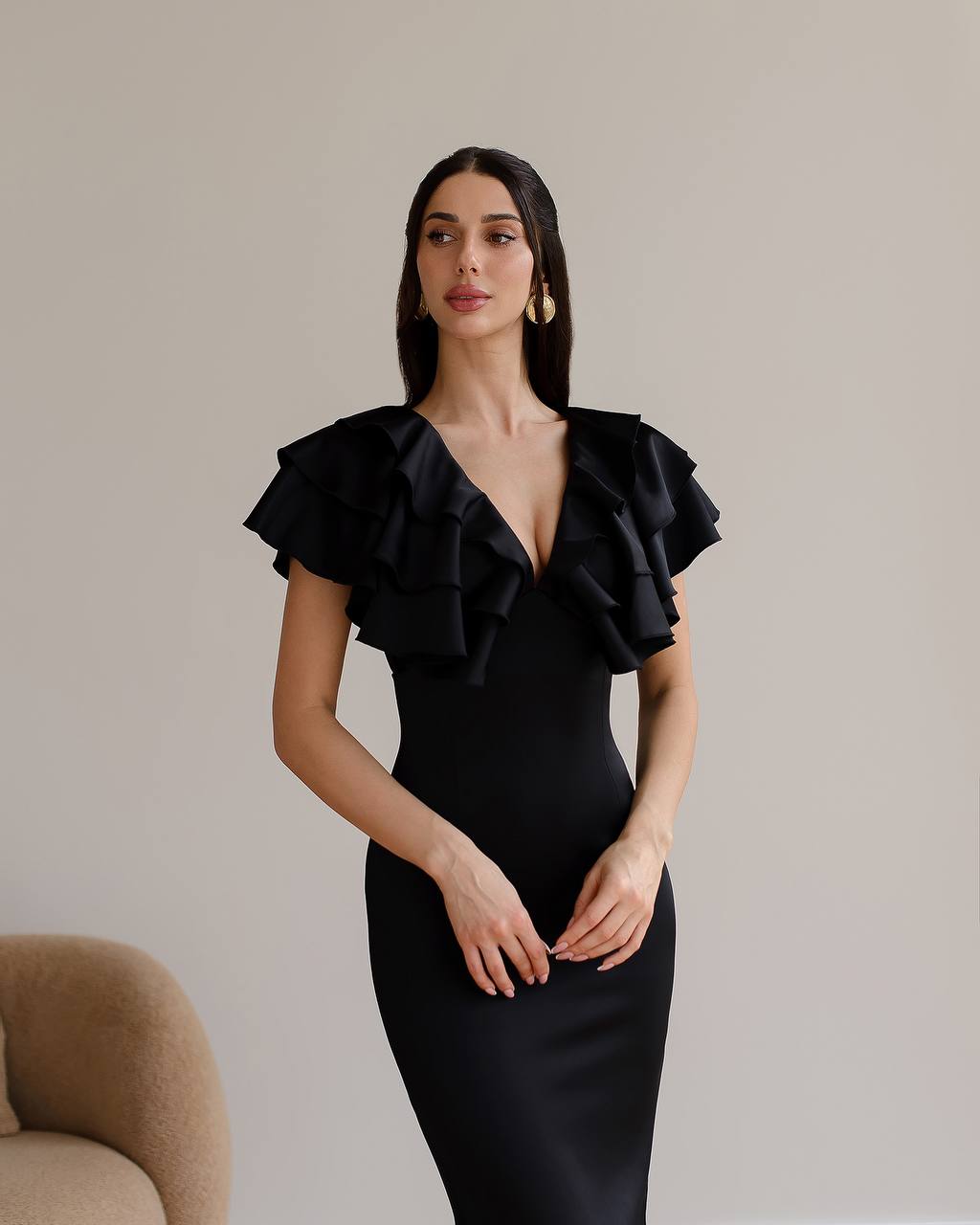 Woman wearing a black dress with ruffled shoulders against a neutral background