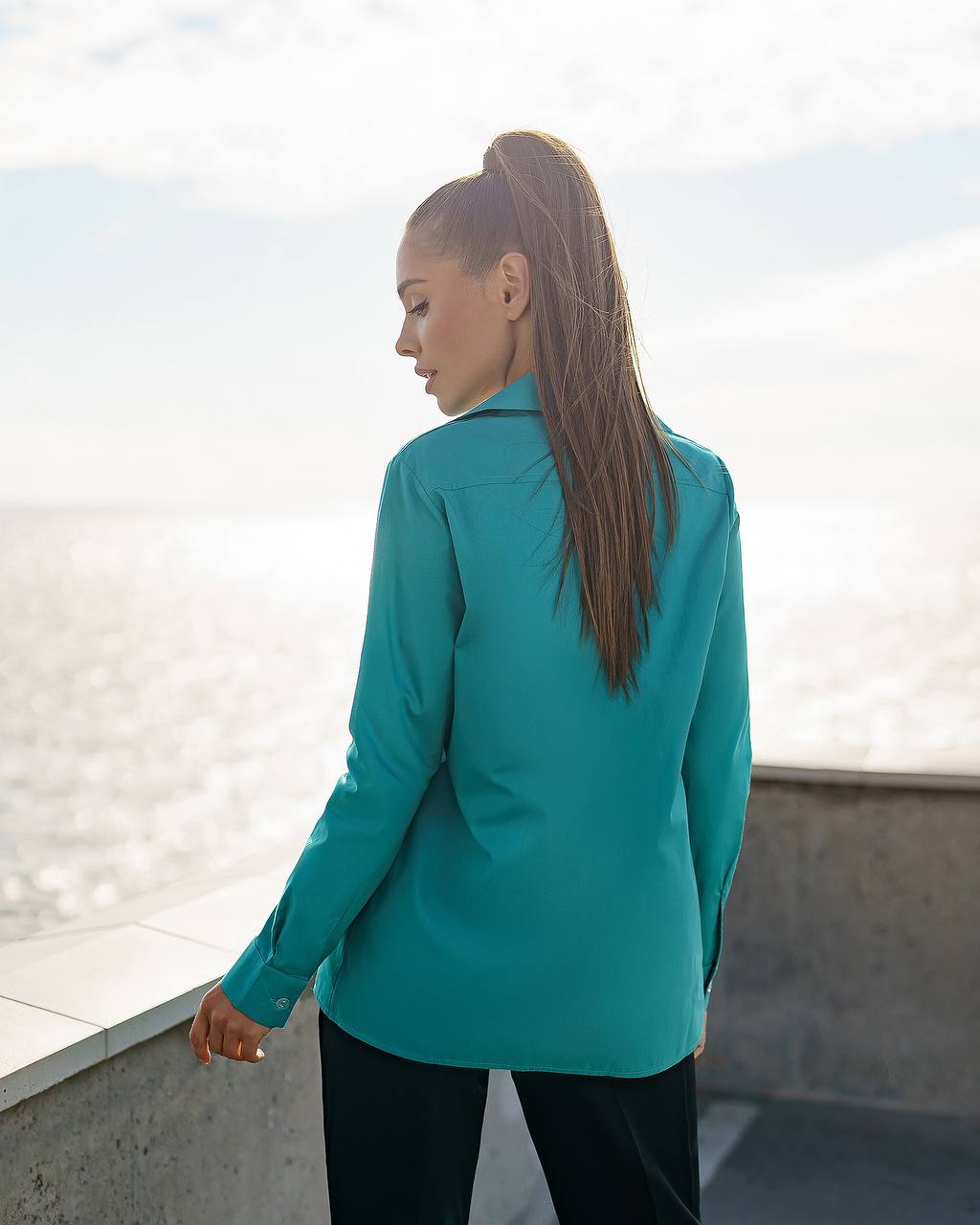 Person wearing a teal blazer standing on a rooftop with a cityscape background
