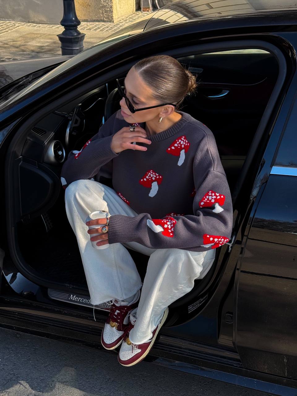 Person sitting in an open car door wearing a sweater with mushroom patterns.
