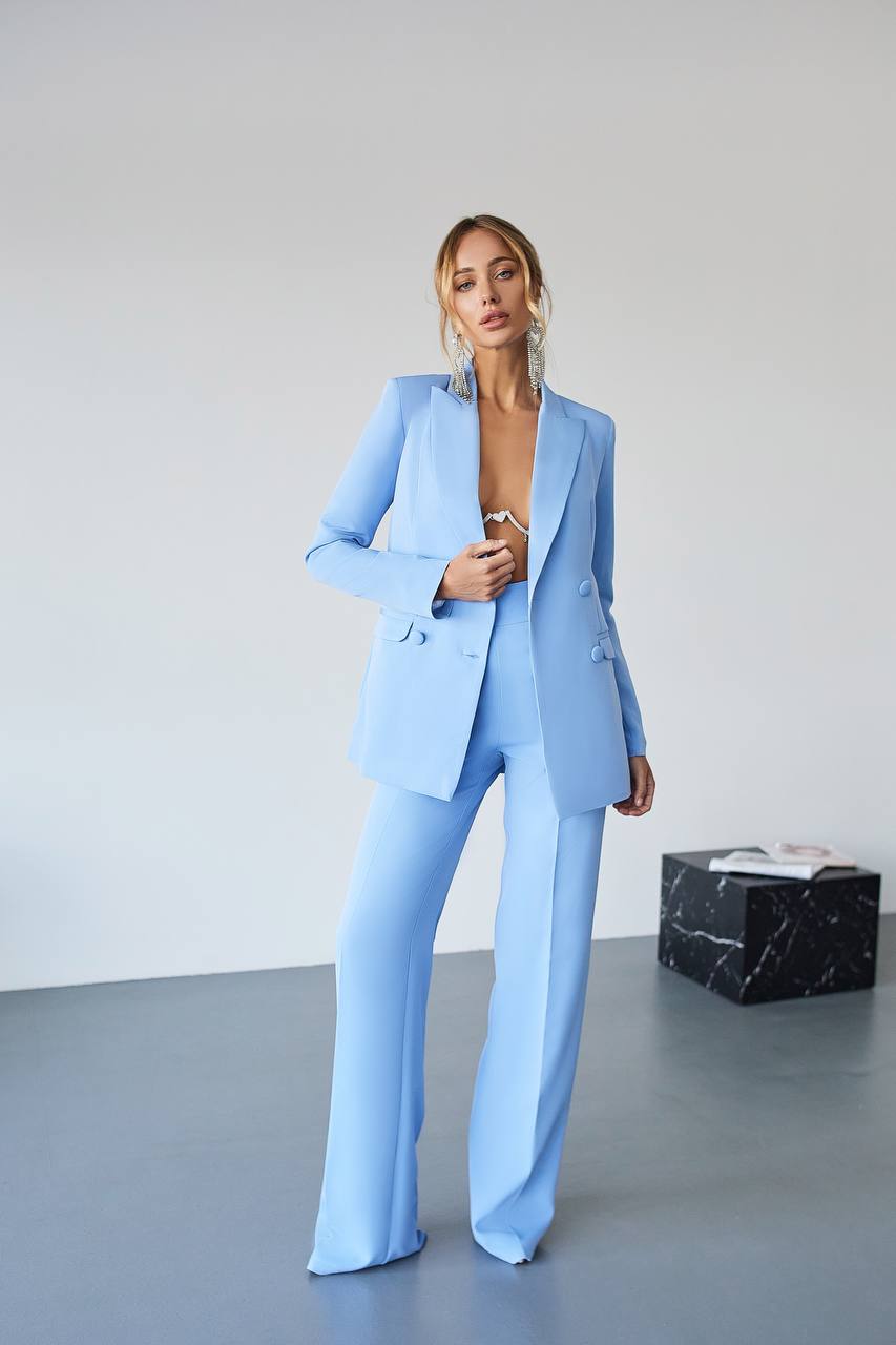 Woman wearing a light blue suit standing against a plain background