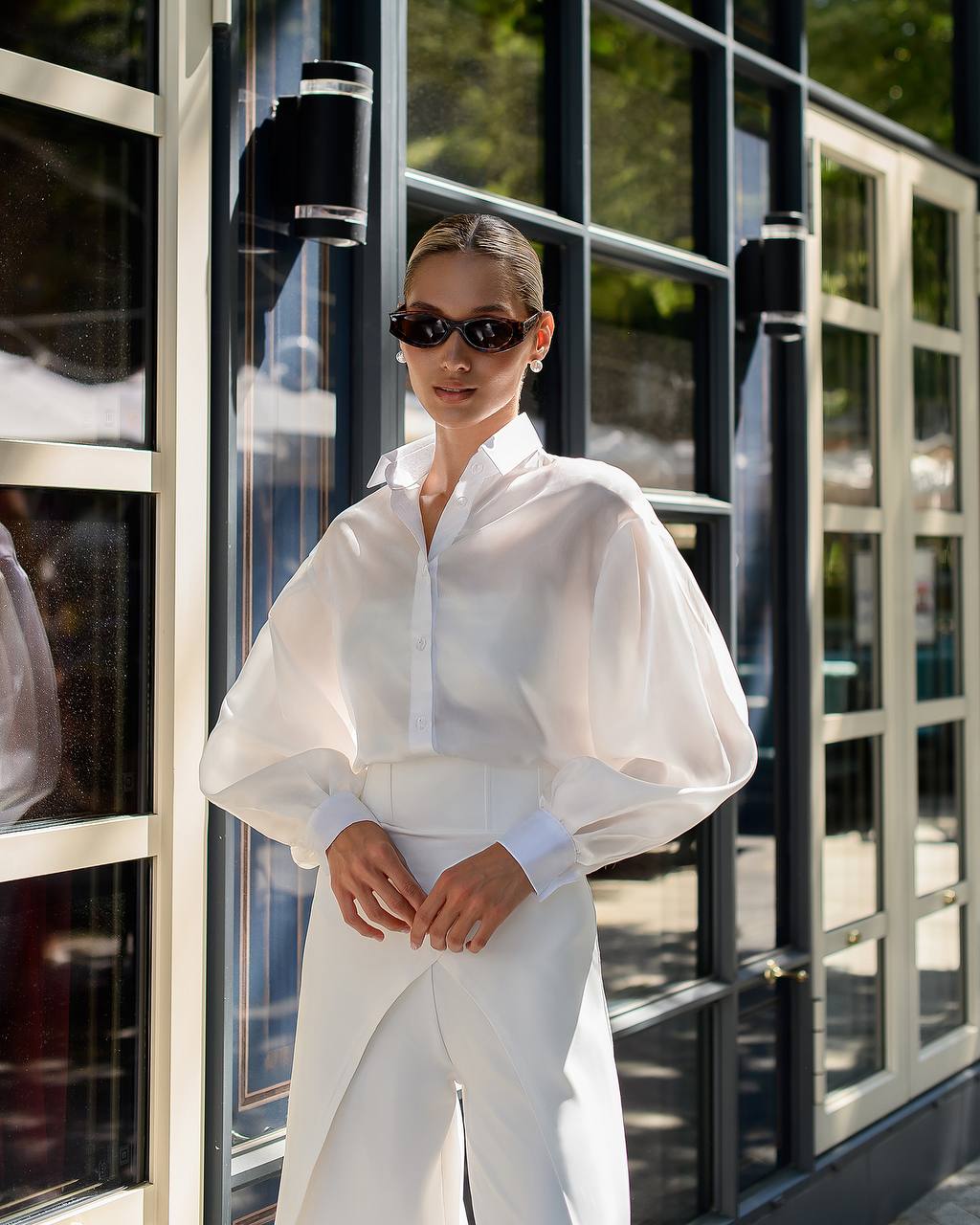 Person wearing a white outfit with puffed sleeves in front of a glass building.