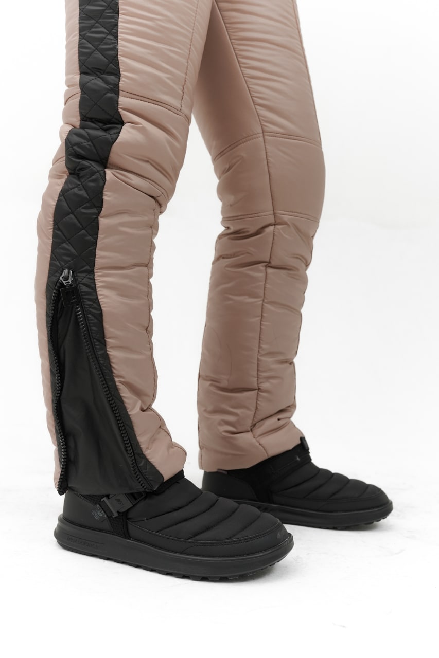 Black winter boots worn with beige pants on a white background