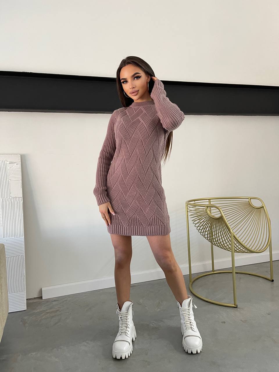 Woman wearing a pink knitted dress with white high-top sneakers in a minimalistic room.