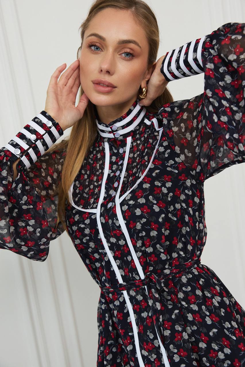 Woman wearing a black floral dress with red and gray accents against a white background