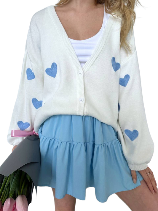 Person wearing a white cardigan with blue heart patterns and a light blue skirt.