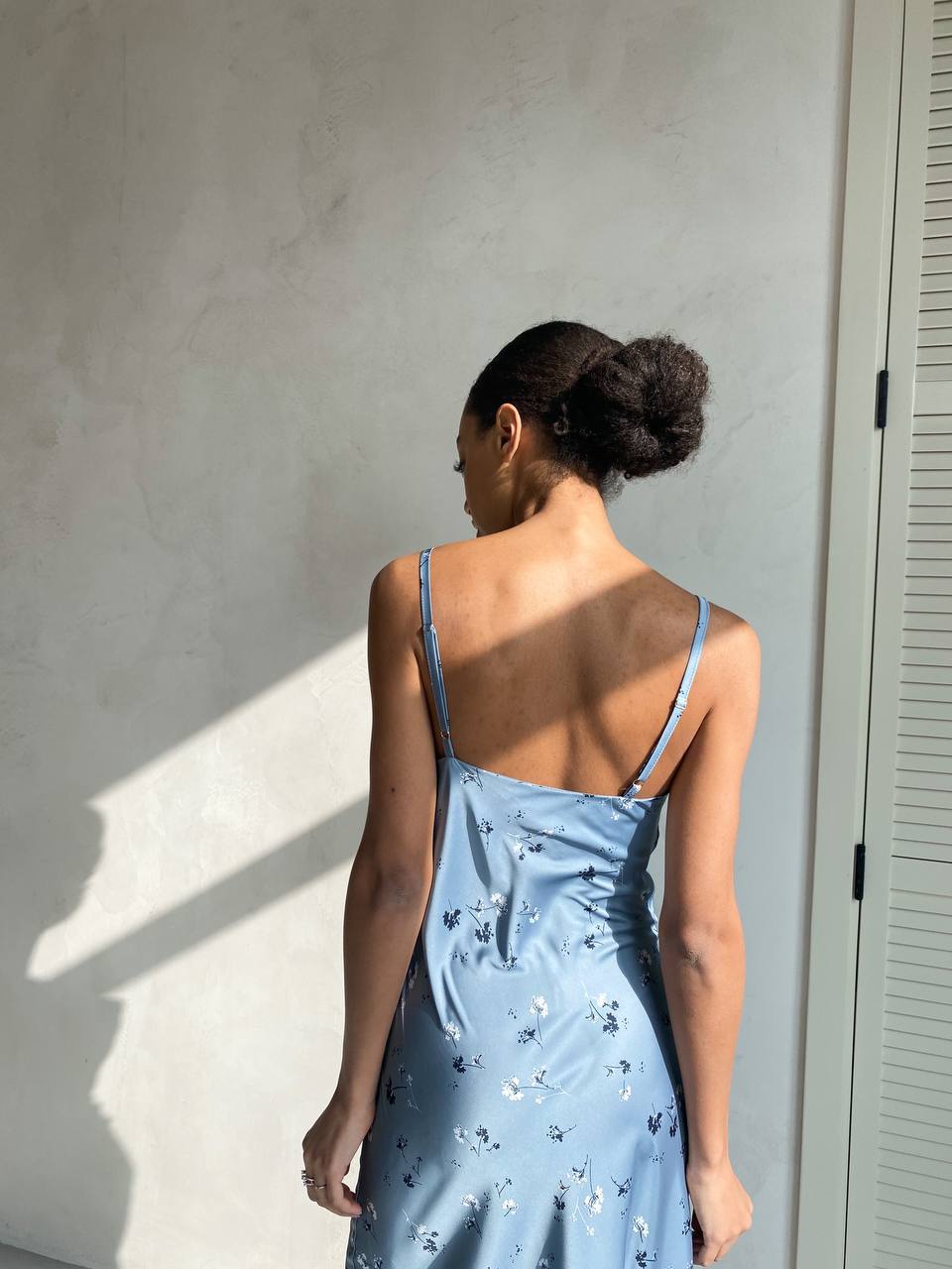 Woman wearing a light blue floral dress against a neutral wall.