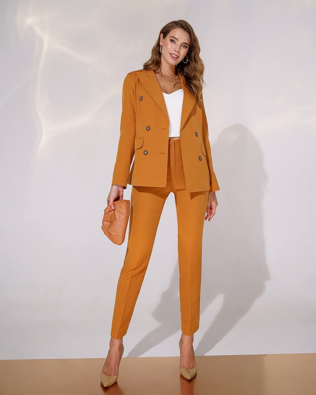 Woman wearing a mustard yellow suit with a white top against a plain background