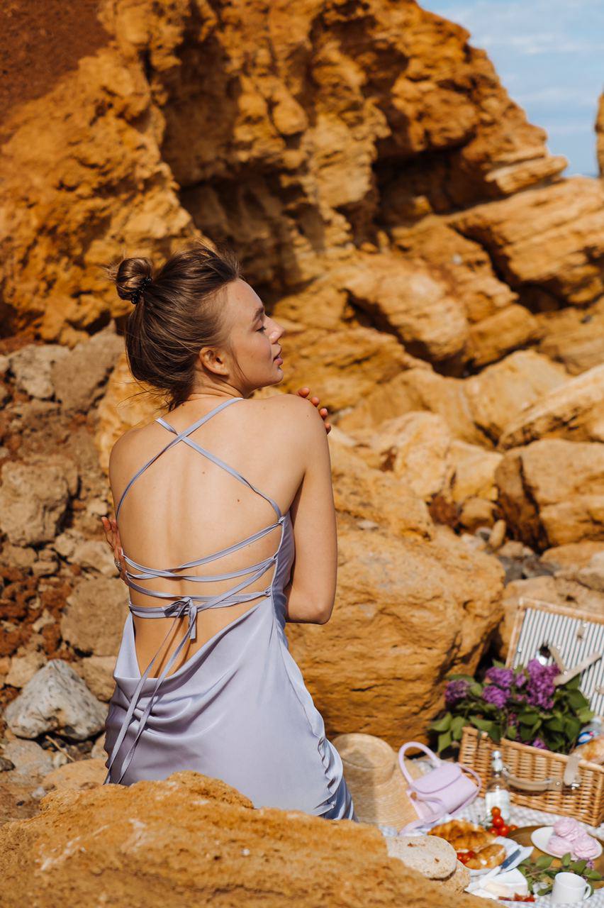 Woman in a strappy dress standing on a rocky beach with a picnic setup.