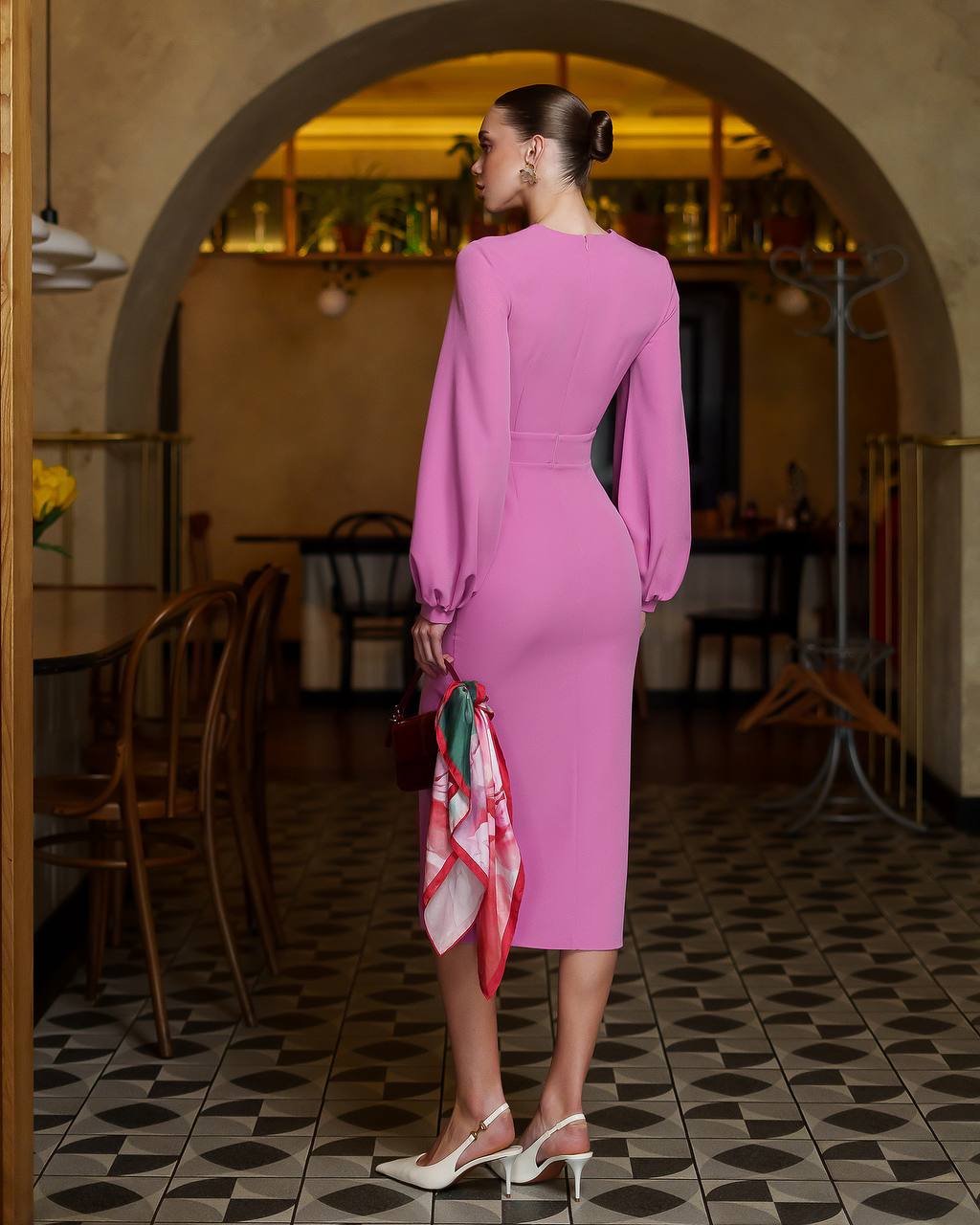 Woman in a pink dress standing in a restaurant with a patterned floor.