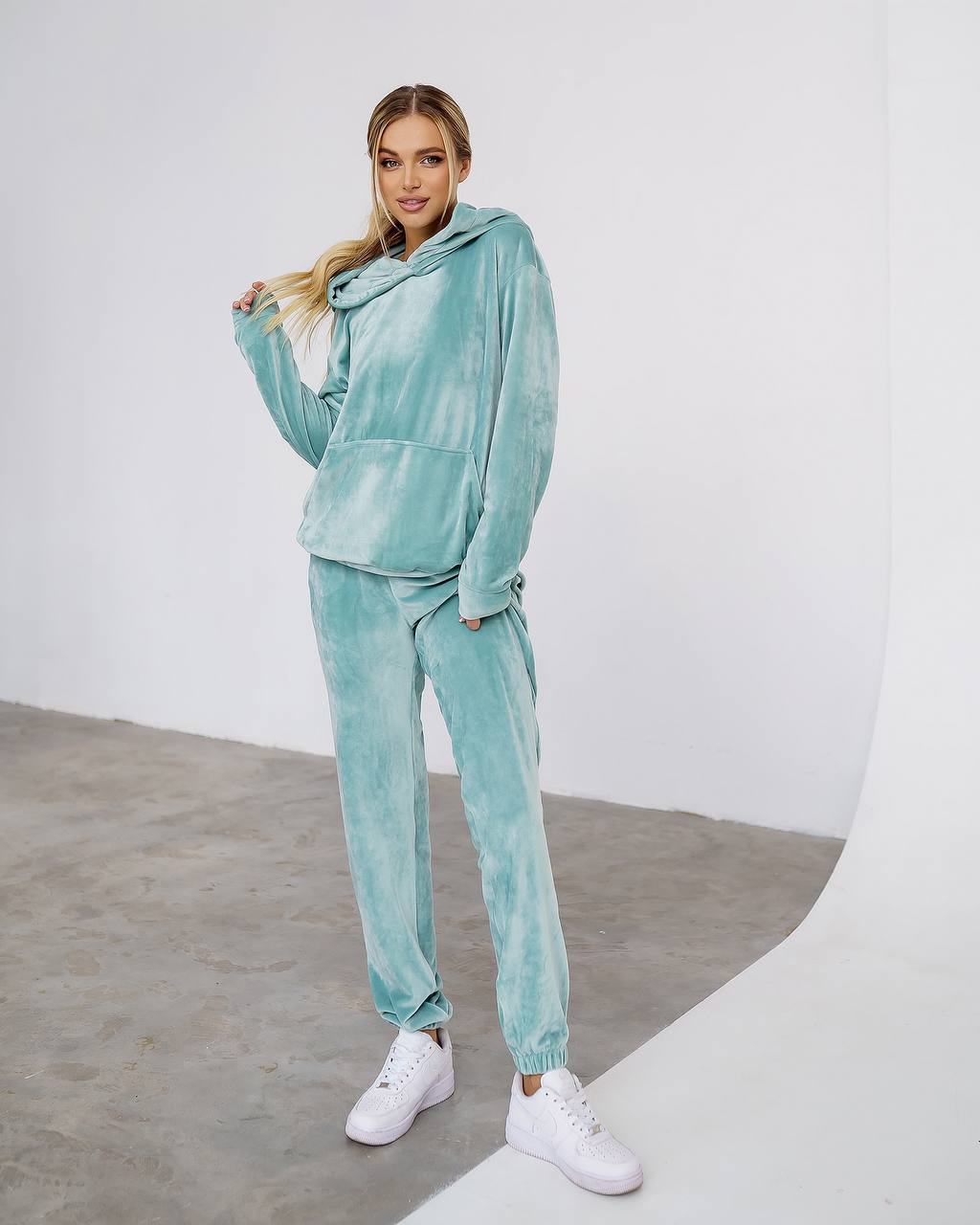 Woman wearing a teal tracksuit with white sneakers on a plain background