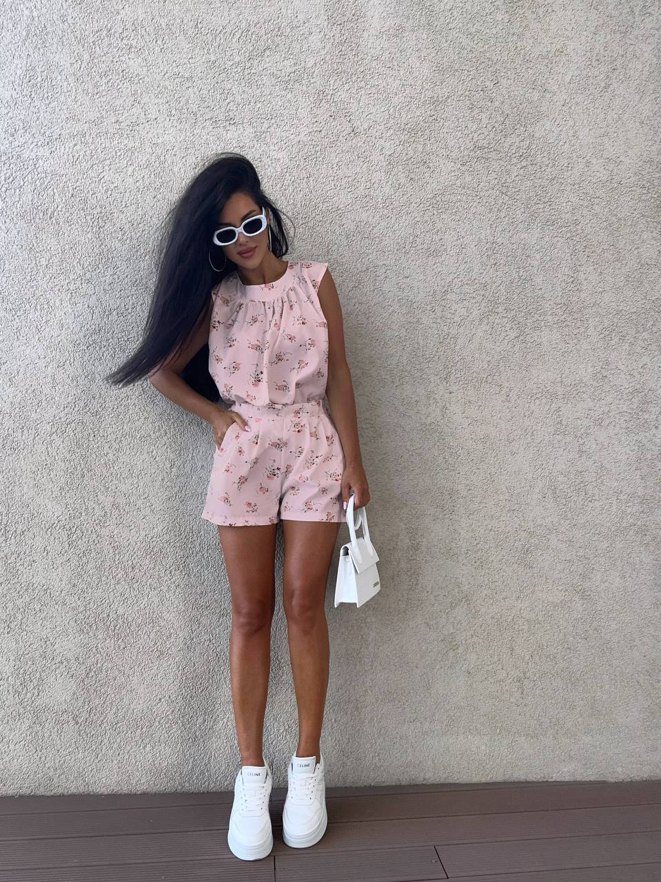 Woman in a pink floral outfit standing against a textured wall.