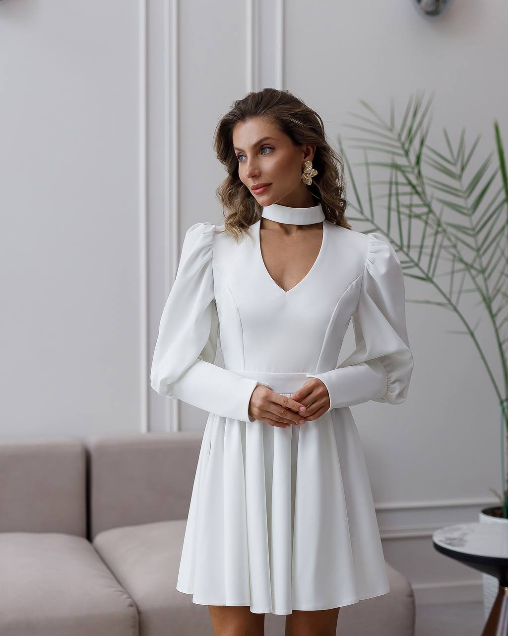 Woman wearing a white dress with long sleeves in an indoor setting.
