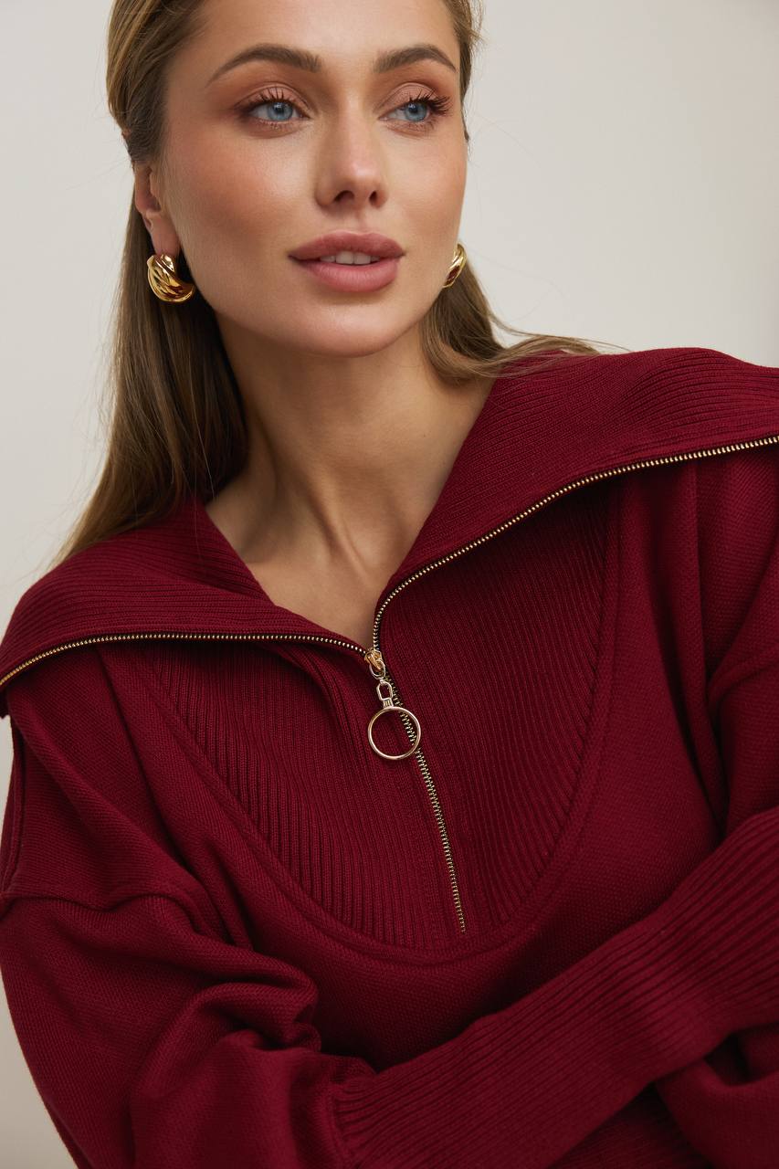 Woman wearing a burgundy sweater with a gold zipper against a neutral background
