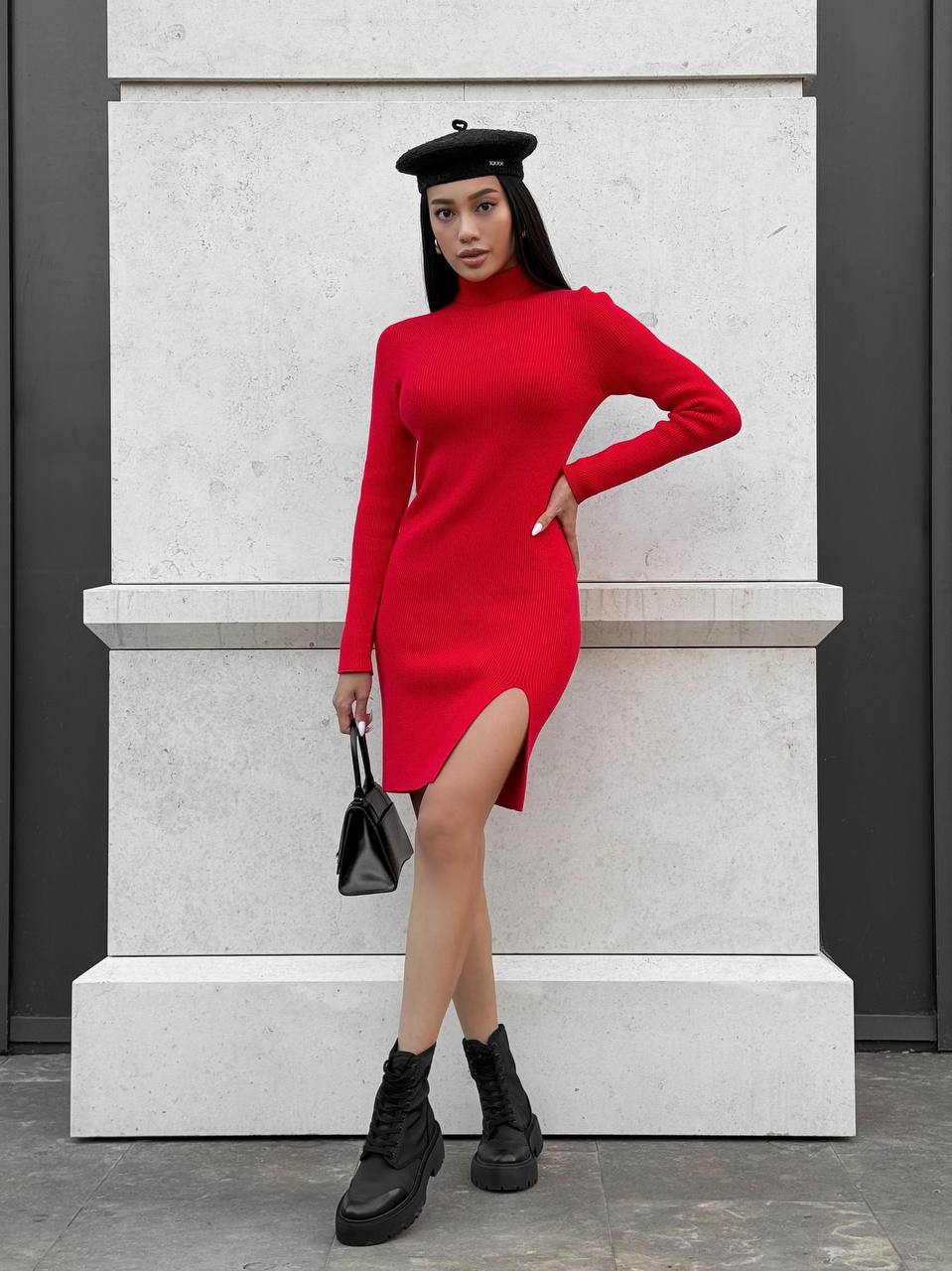 Woman in a red dress with a black beret and boots standing against a light-colored wall.