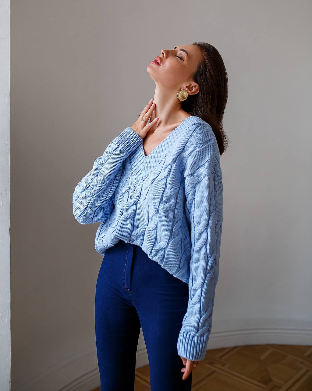 Woman wearing a light blue cable knit sweater and dark blue pants against a neutral wall.