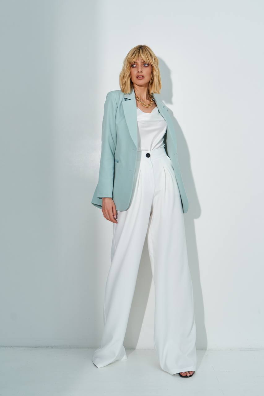 Woman wearing a light blue blazer, white top, and white pants against a white background
