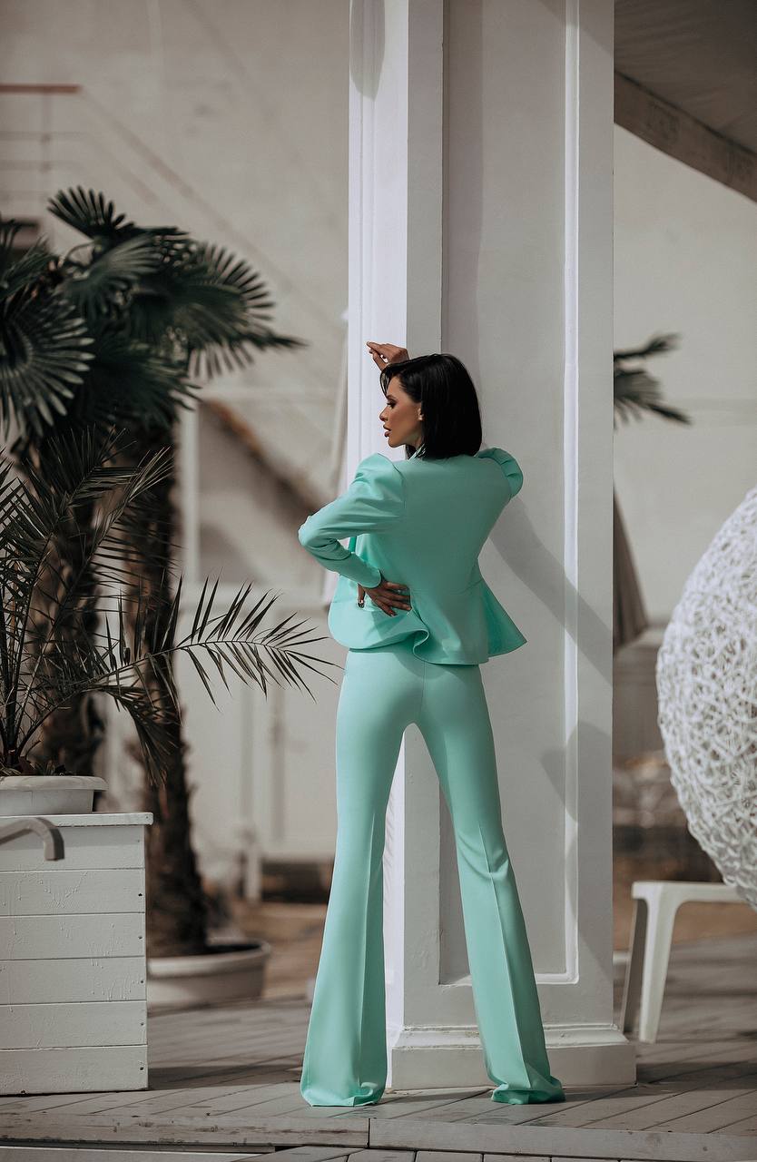 Woman in a teal outfit standing in a modern indoor setting with plants and architectural elements.