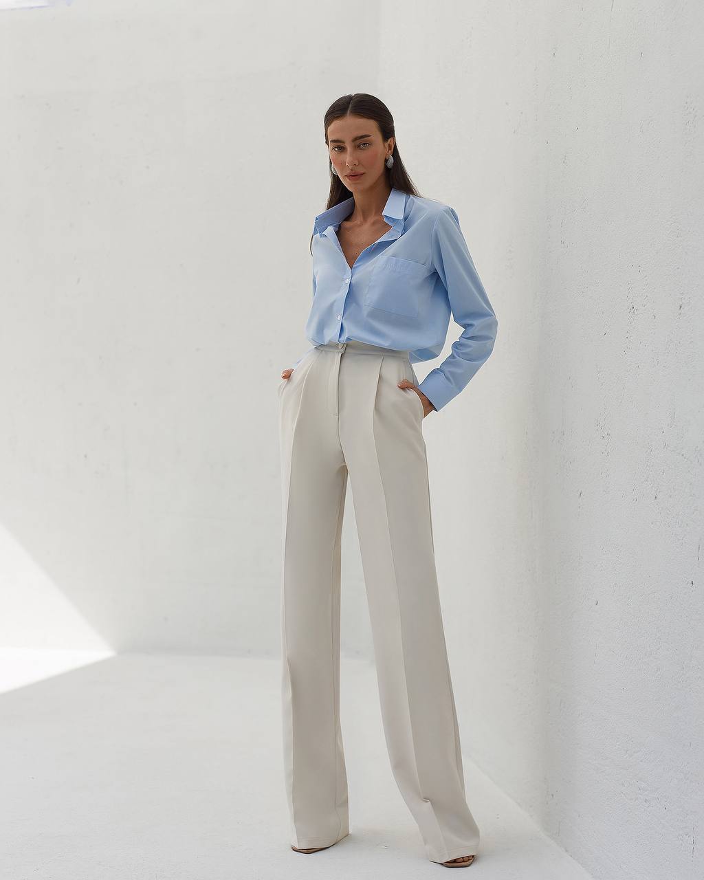 Woman wearing a light blue shirt and beige pants against a white background