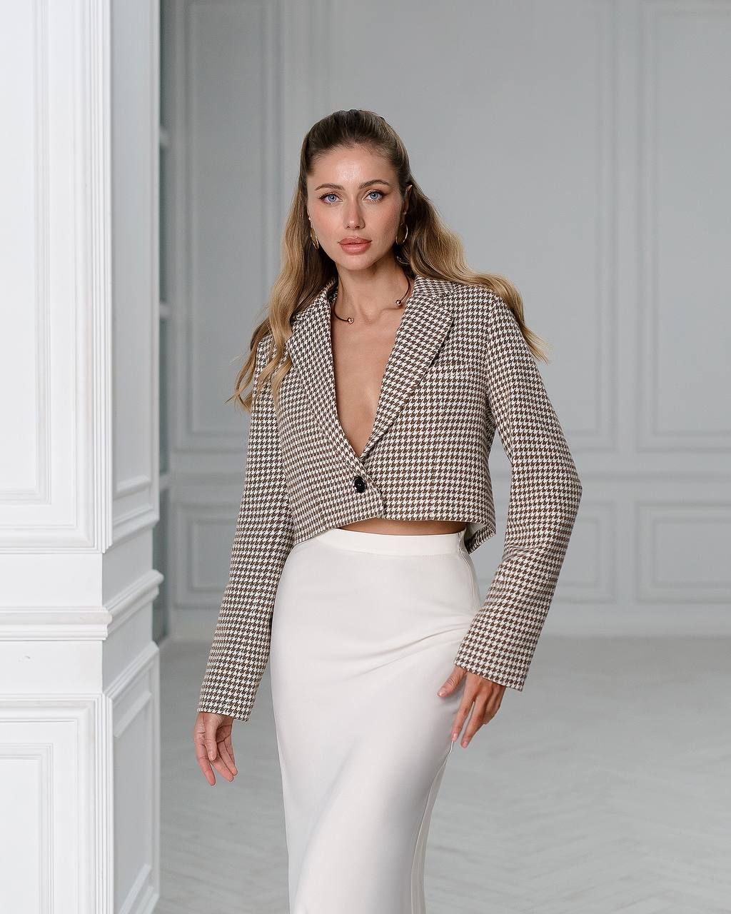 Woman wearing a checkered blazer and white pants in a neutral setting