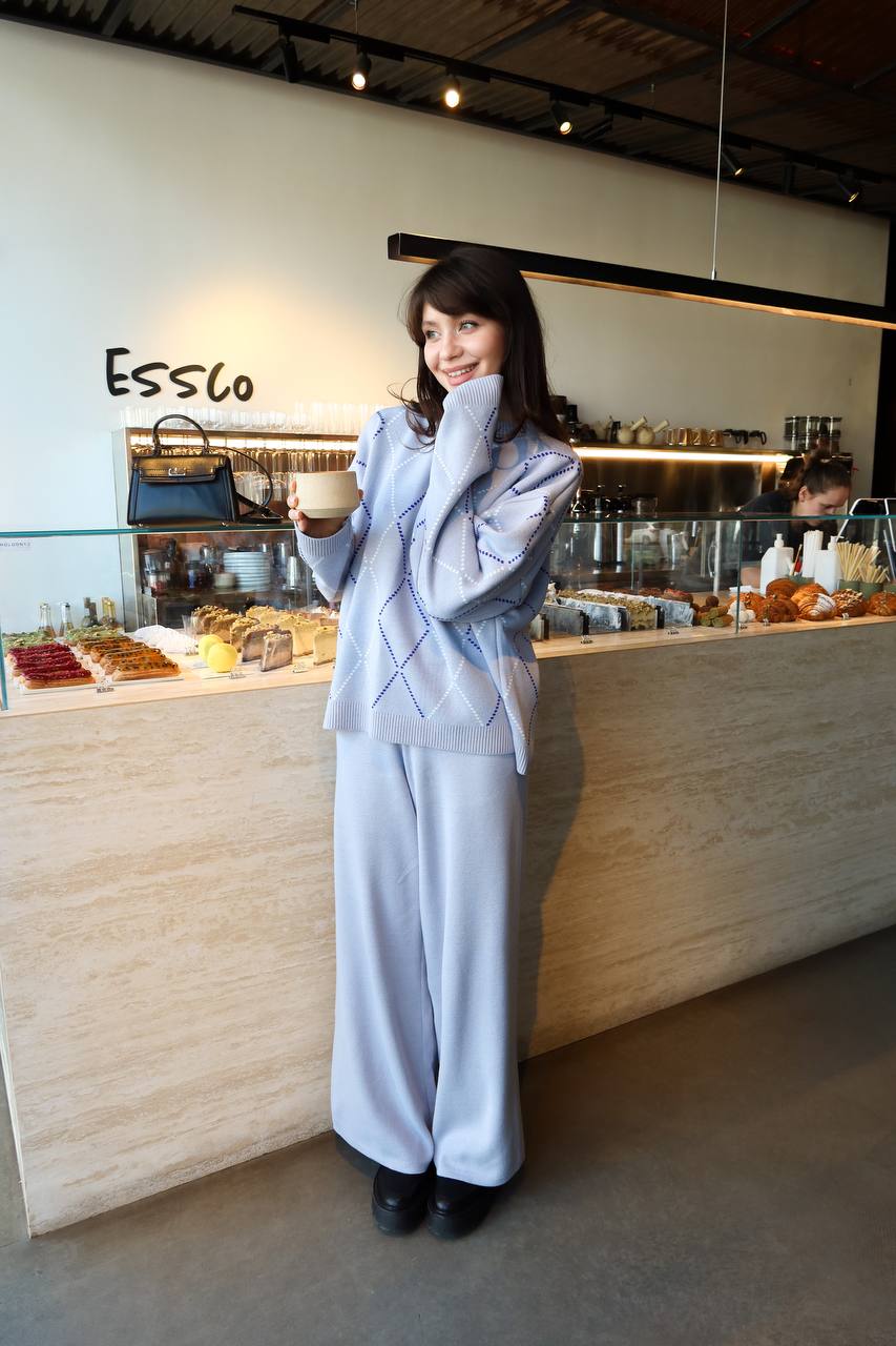 Woman in a light blue suit standing in front of a cafe counter with 'Essco' branding.