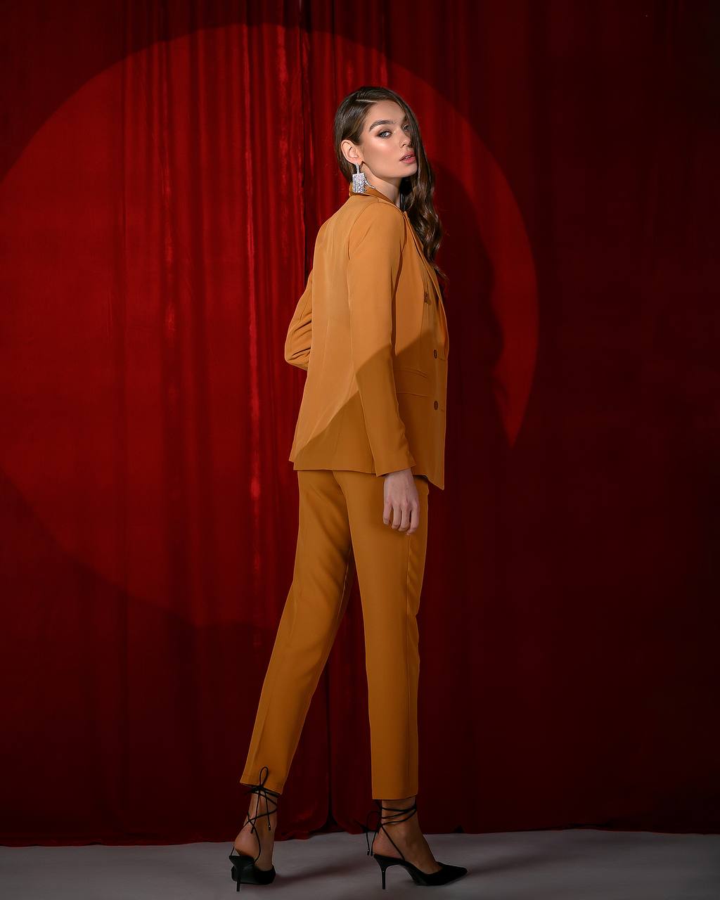 Woman in a mustard yellow outfit standing against a red curtain backdrop