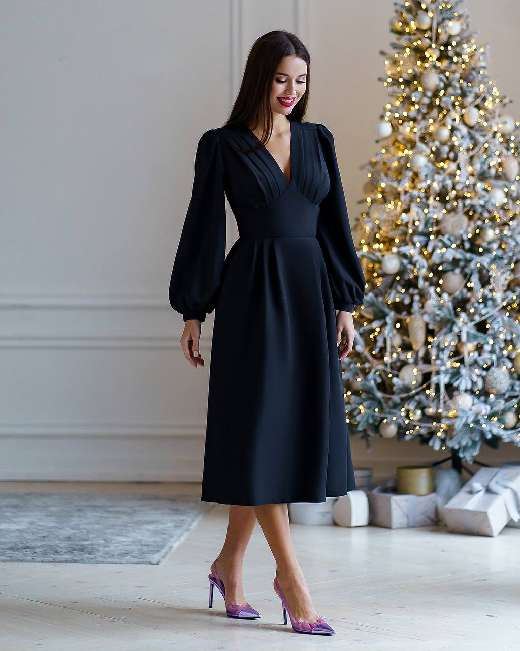 Woman in a black dress standing in front of a decorated Christmas tree.
