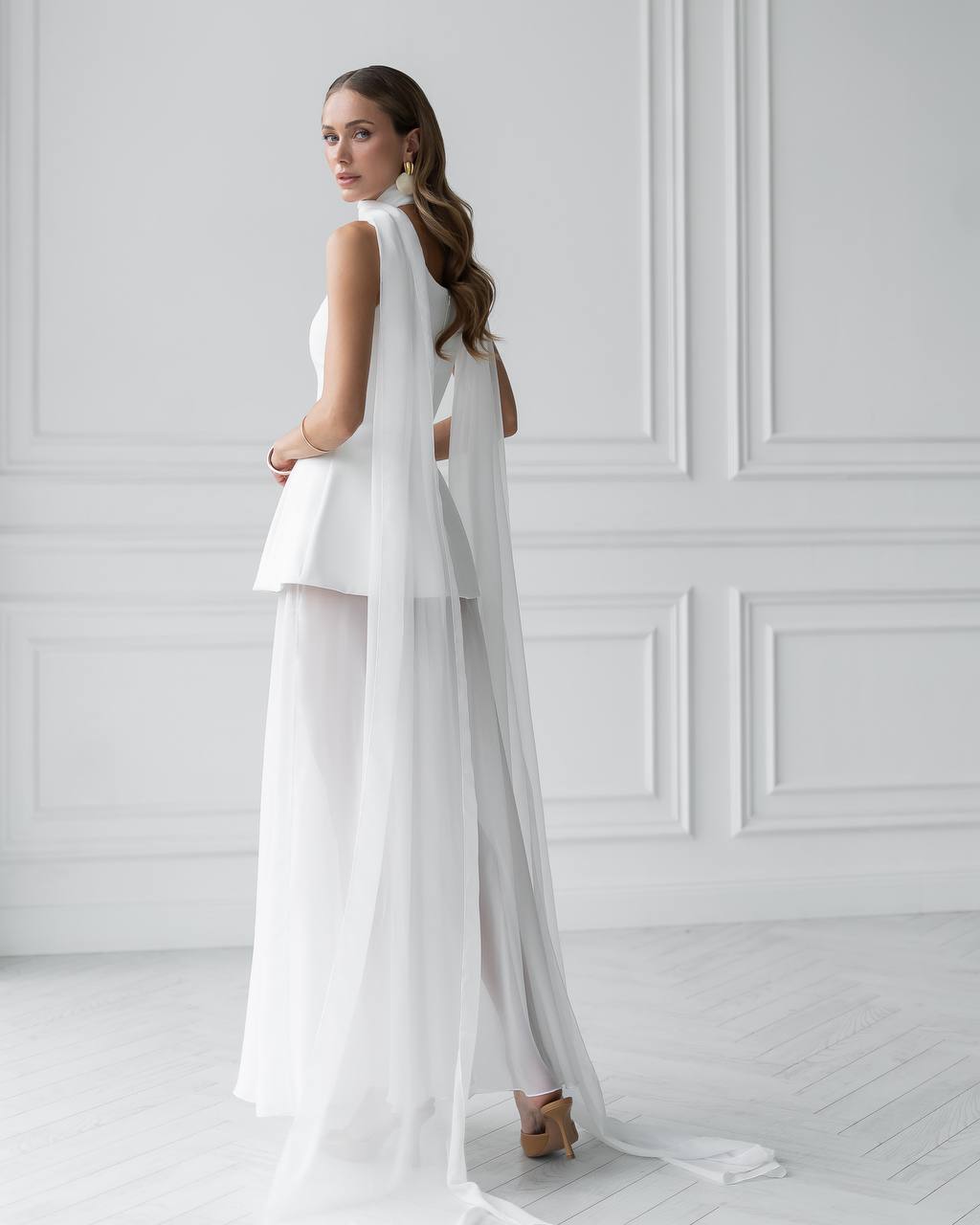 Woman wearing a white bridal outfit with a long train in a minimalistic setting