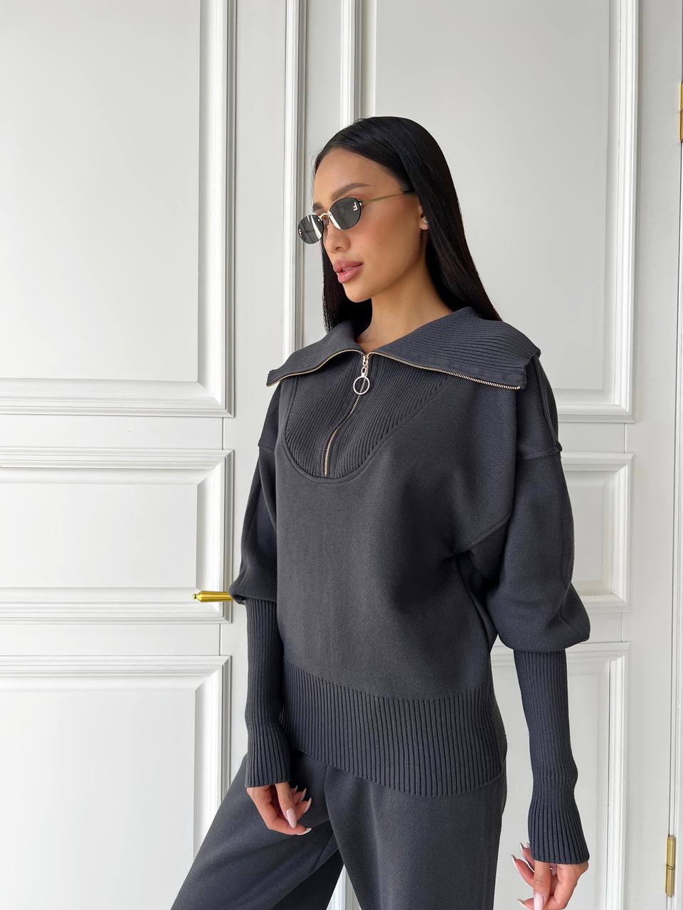 Woman wearing a dark gray sweater with a textured collar in front of a white paneled door.