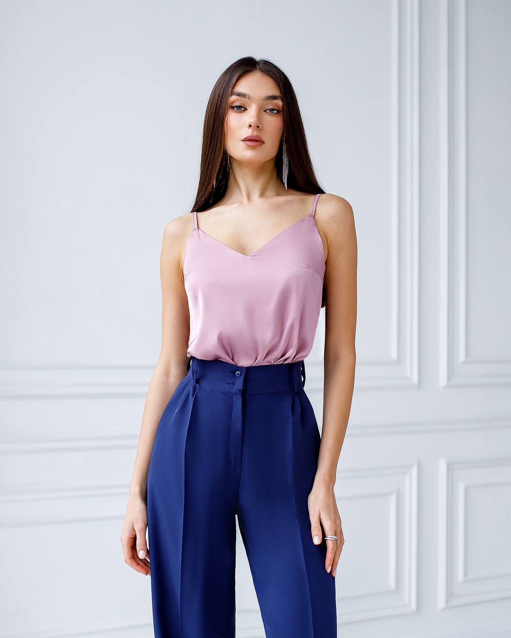 Woman wearing a pink top and blue pants against a white wall