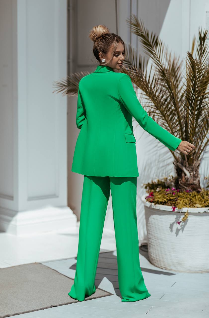 Person wearing a green suit standing outdoors with plants in the background