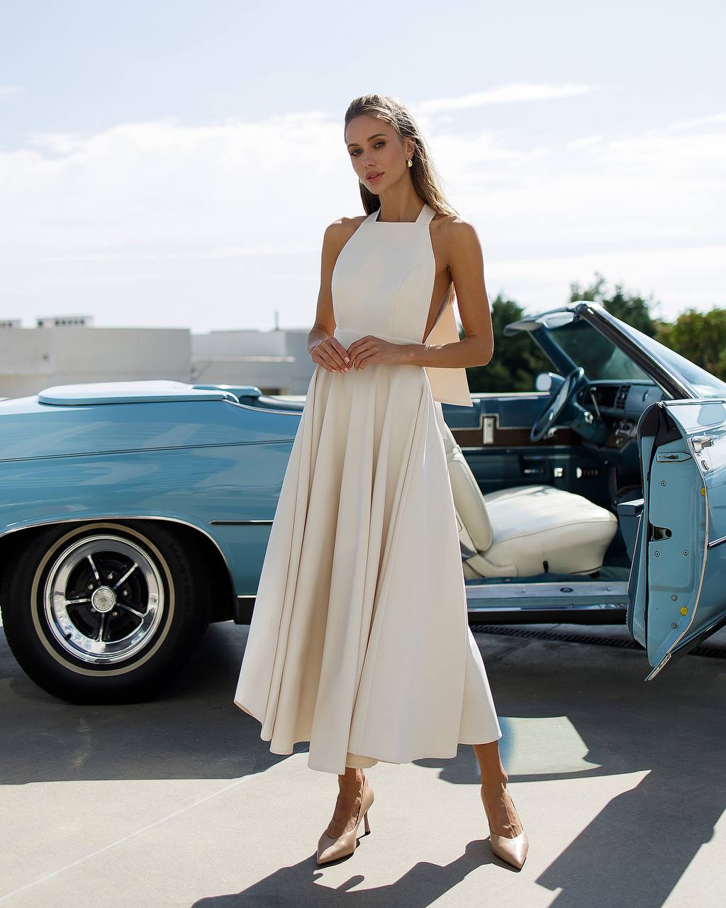 Woman in a white dress standing next to a classic blue car