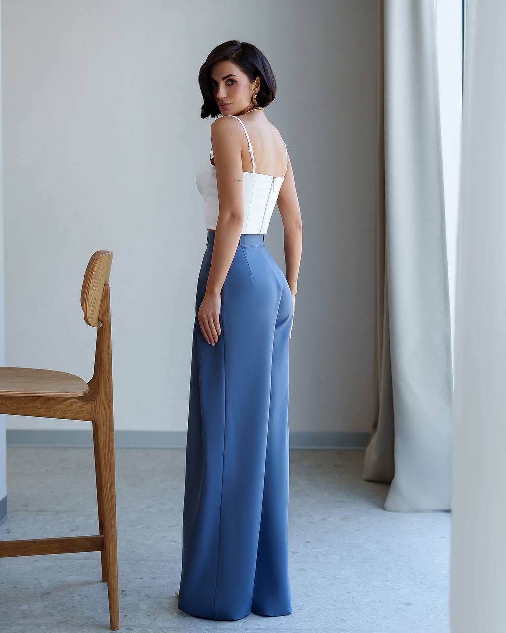 Woman wearing a white top and blue pants in a minimalistic room.