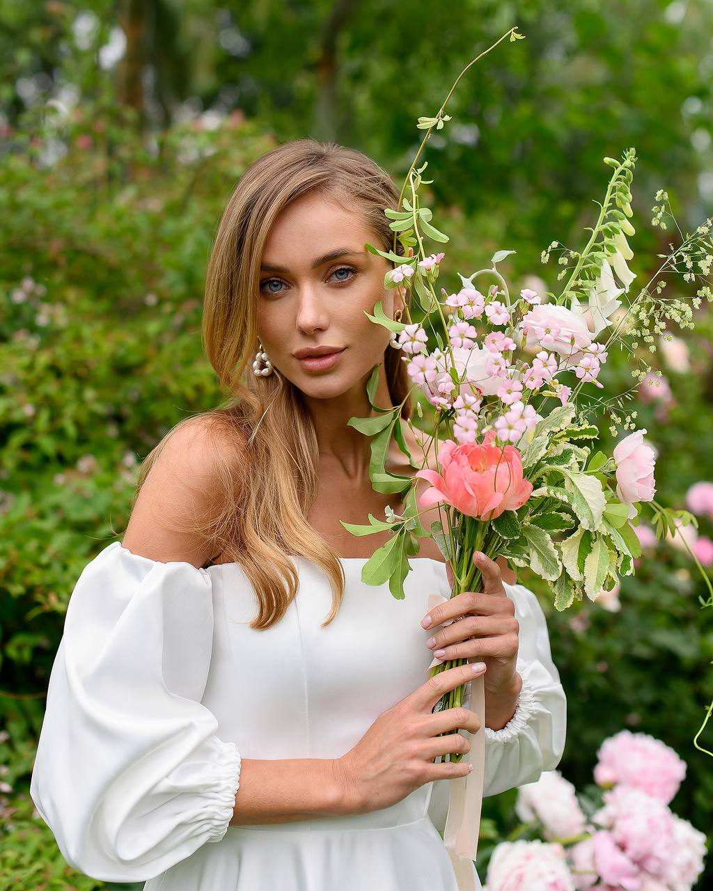 Woman in a white dress holding a bouquet of flowers in a garden setting