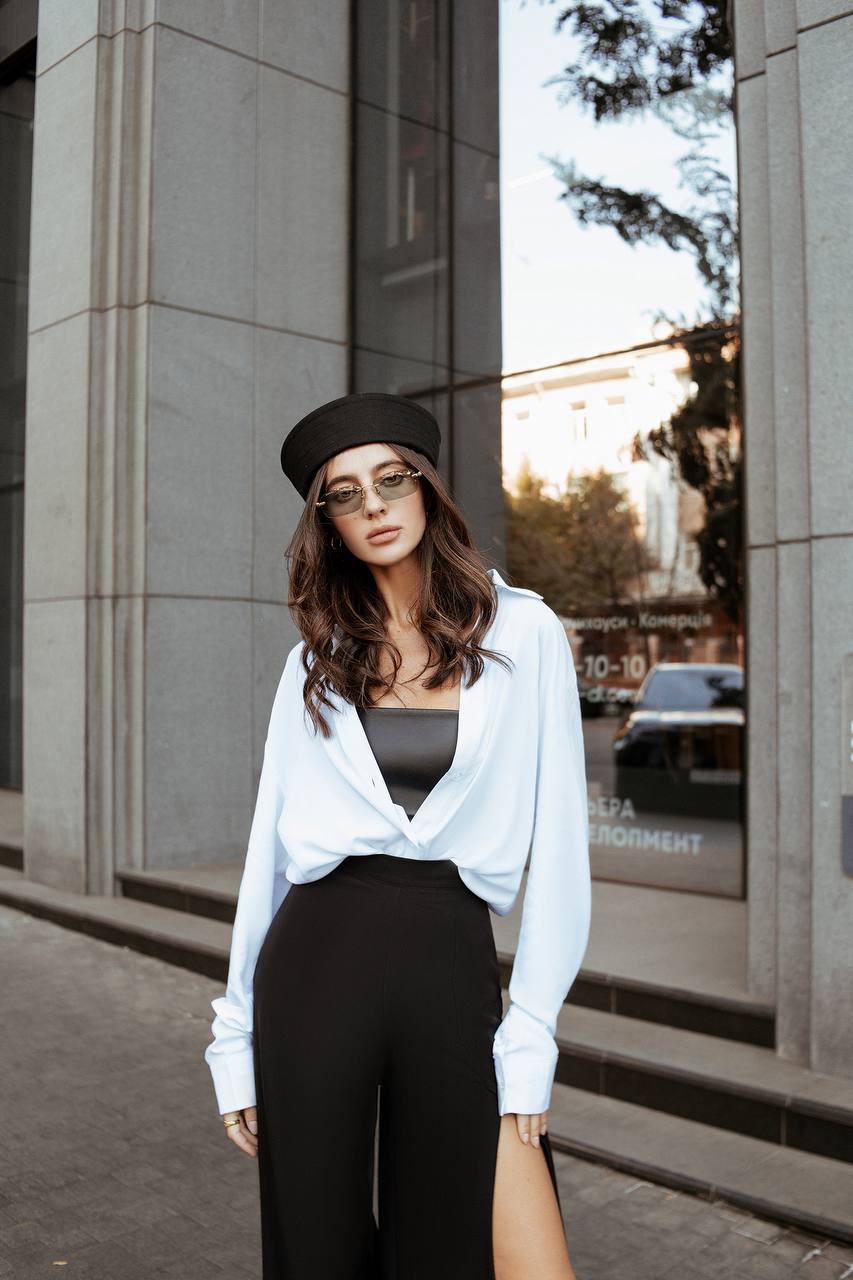 Woman wearing a white blouse and black pants standing on a street.